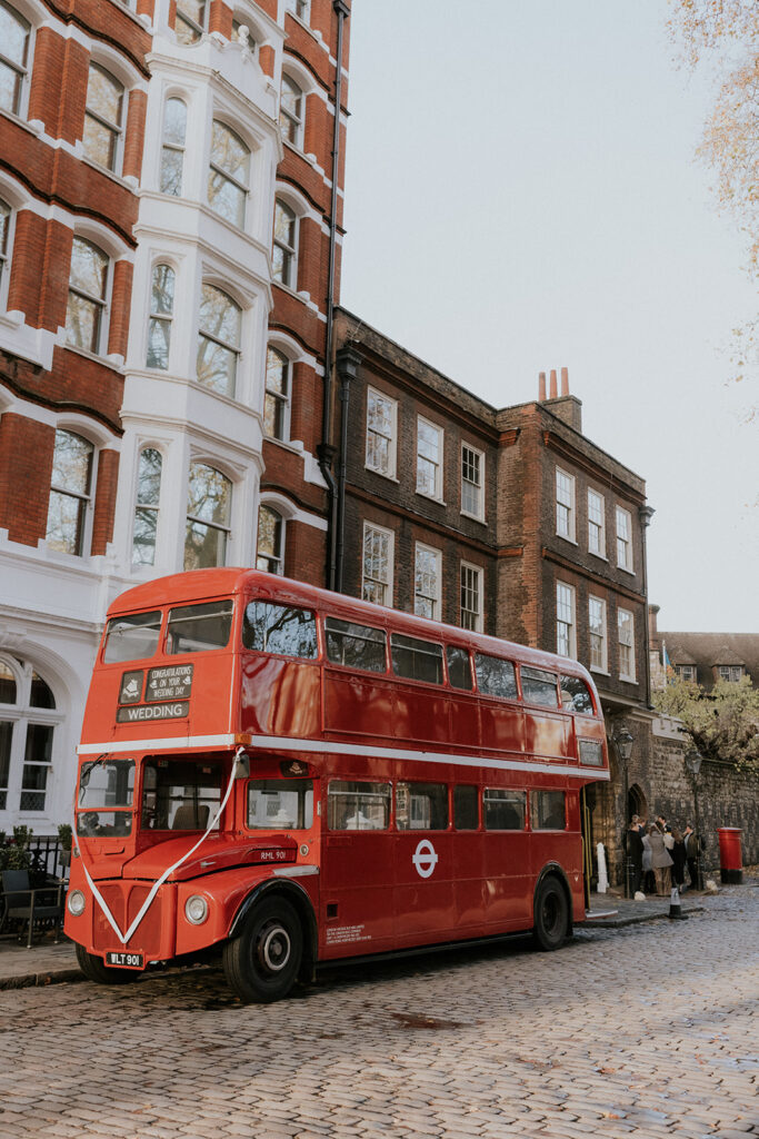 A bright red double-decker bus parked outside, ready to transport wedding guests to the charterhouse.