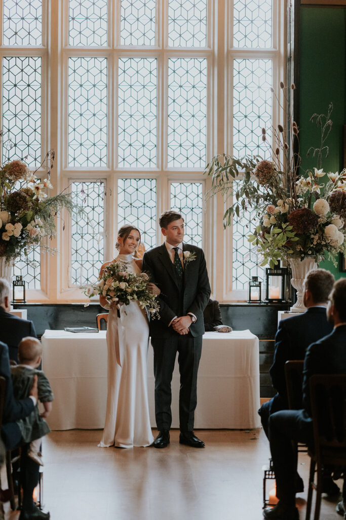 The wedding ceremony in progress with guests seated in rows and the couple exchanging vows at the front, under a decorative arch.