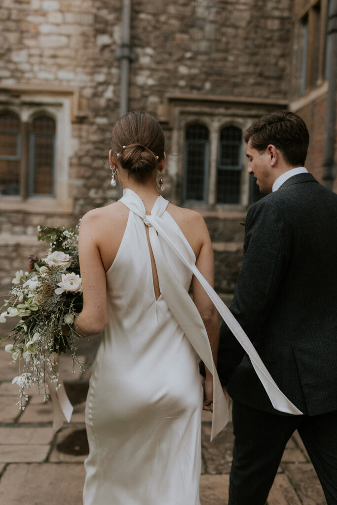 Newlyweds Hugo and Charlotte walking hand-in-hand through the quaint courtyard of their wedding venue