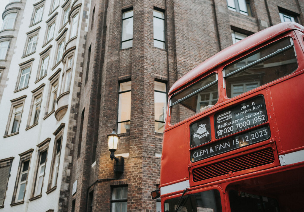 A classic red Routemaster bus with “Clem & Finn 15.12.2023” on the front, transporting the newlyweds from the church to Battersea Arts Centre.