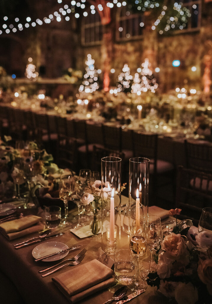 A detailed shot of the wedding table setting, featuring tall candles and delicate floral arrangements, adding warmth and charm to the evening.