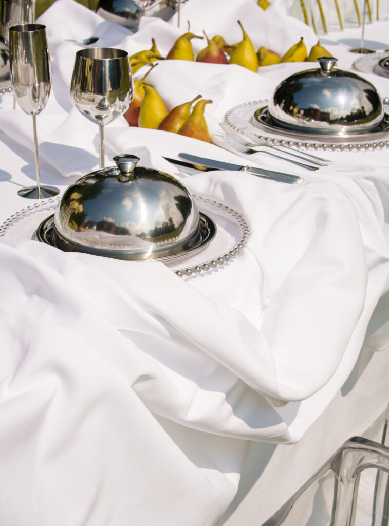 Elegant table setting with silver cloches, champagne flutes, and pears, creating a refined and luxurious dining experience.