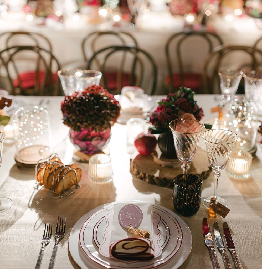 A creative dessert plate with a small card displaying the guest’s name, accented by candlelight and vibrant floral decor on the table.