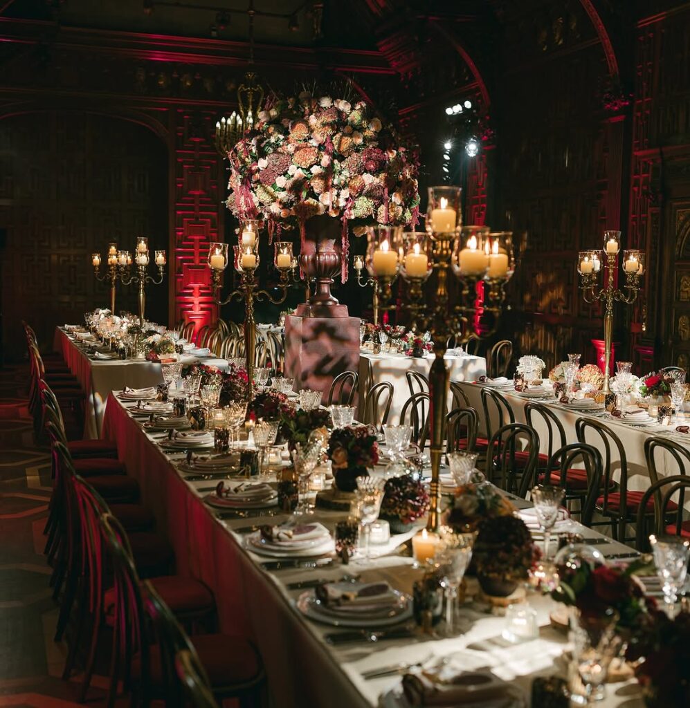 A wide-angle view of a lavish dinner setup at Two Temple Place, with long banquet tables adorned with floral centerpieces, gold candelabras, and soft, romantic lighting.