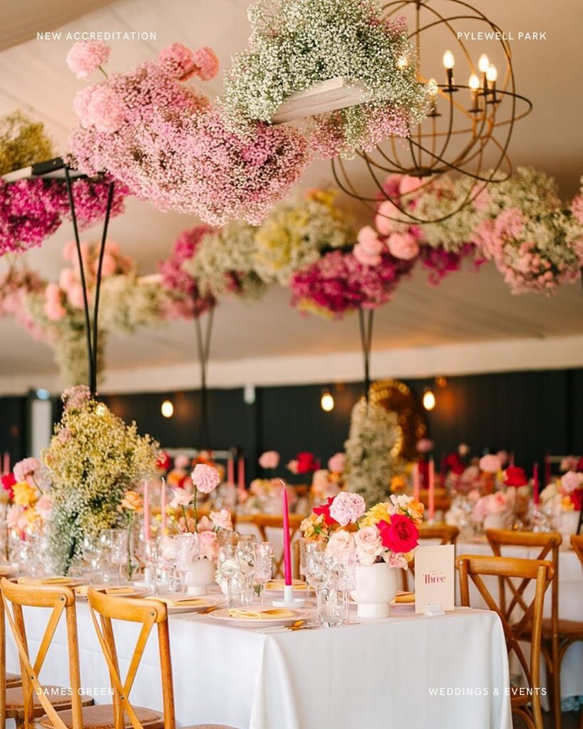 Vibrant hanging floral installation in the marquee at Pylewell Park wedding, featuring pink and pastel blooms above banquet-style tables.