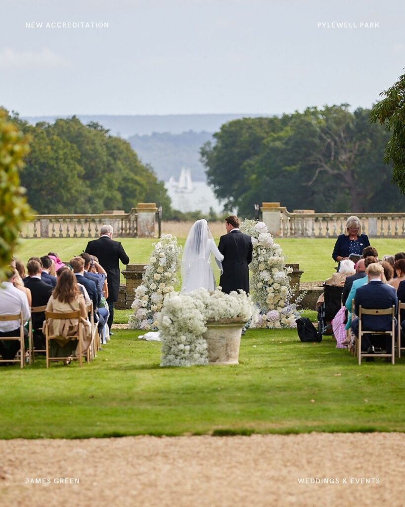 Pylewell Park wedding ceremony setup on the lawn with white florals, guests seated facing the sea and scenic backdrop of sailing boats.