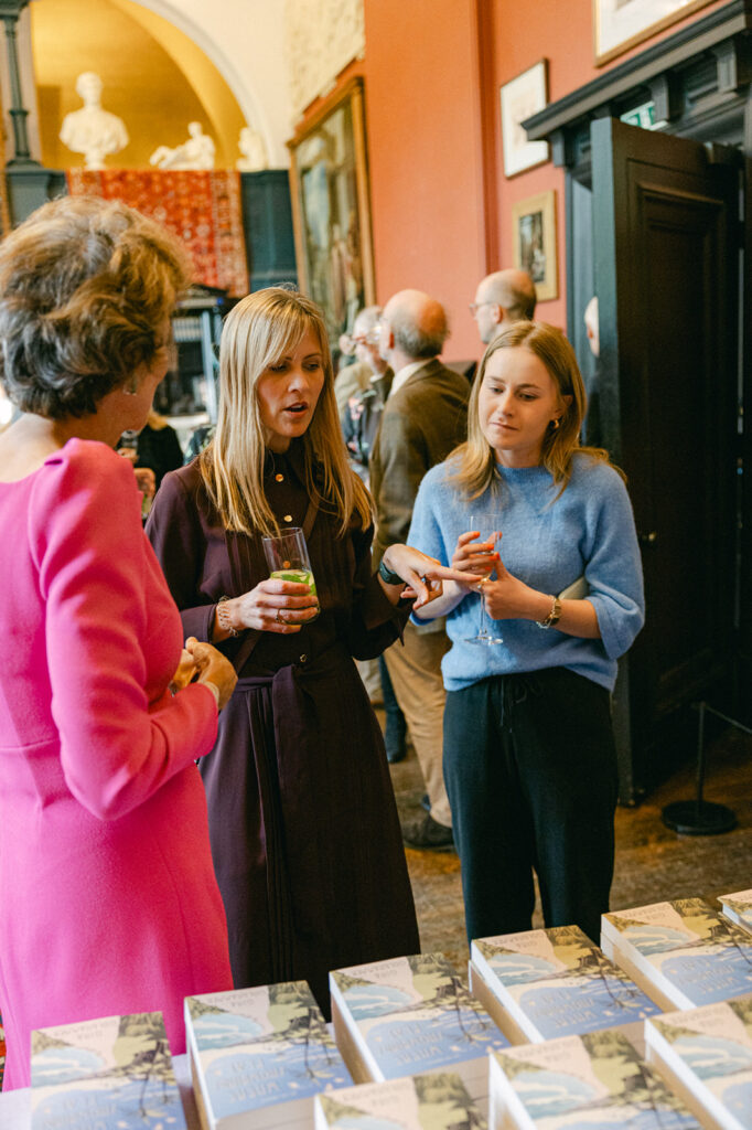 Guests mingle and enjoy drinks beside stacks of Gina Goldhammer’s novel at Leighton House